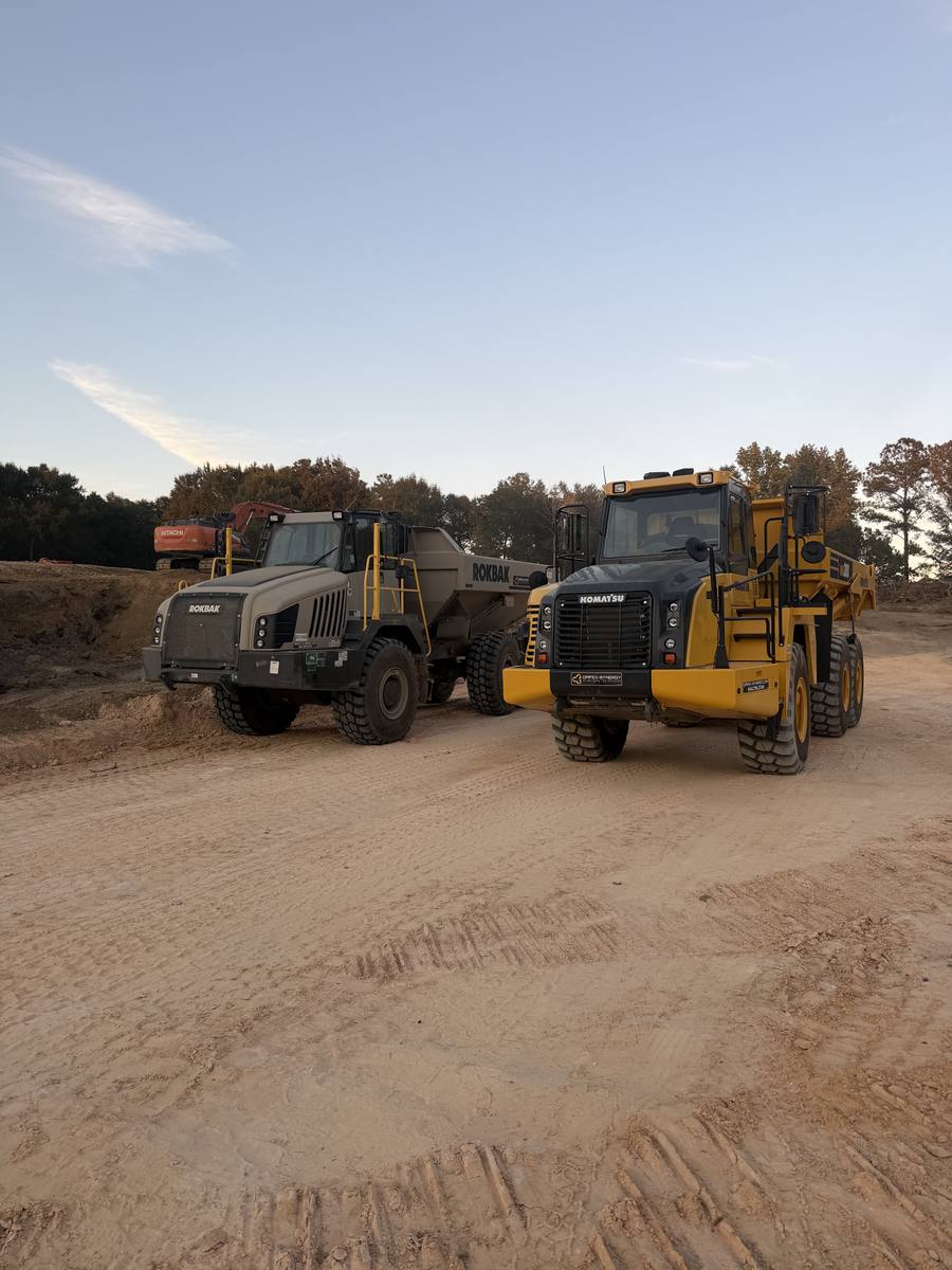 Two articulated haul trucks on a graded site