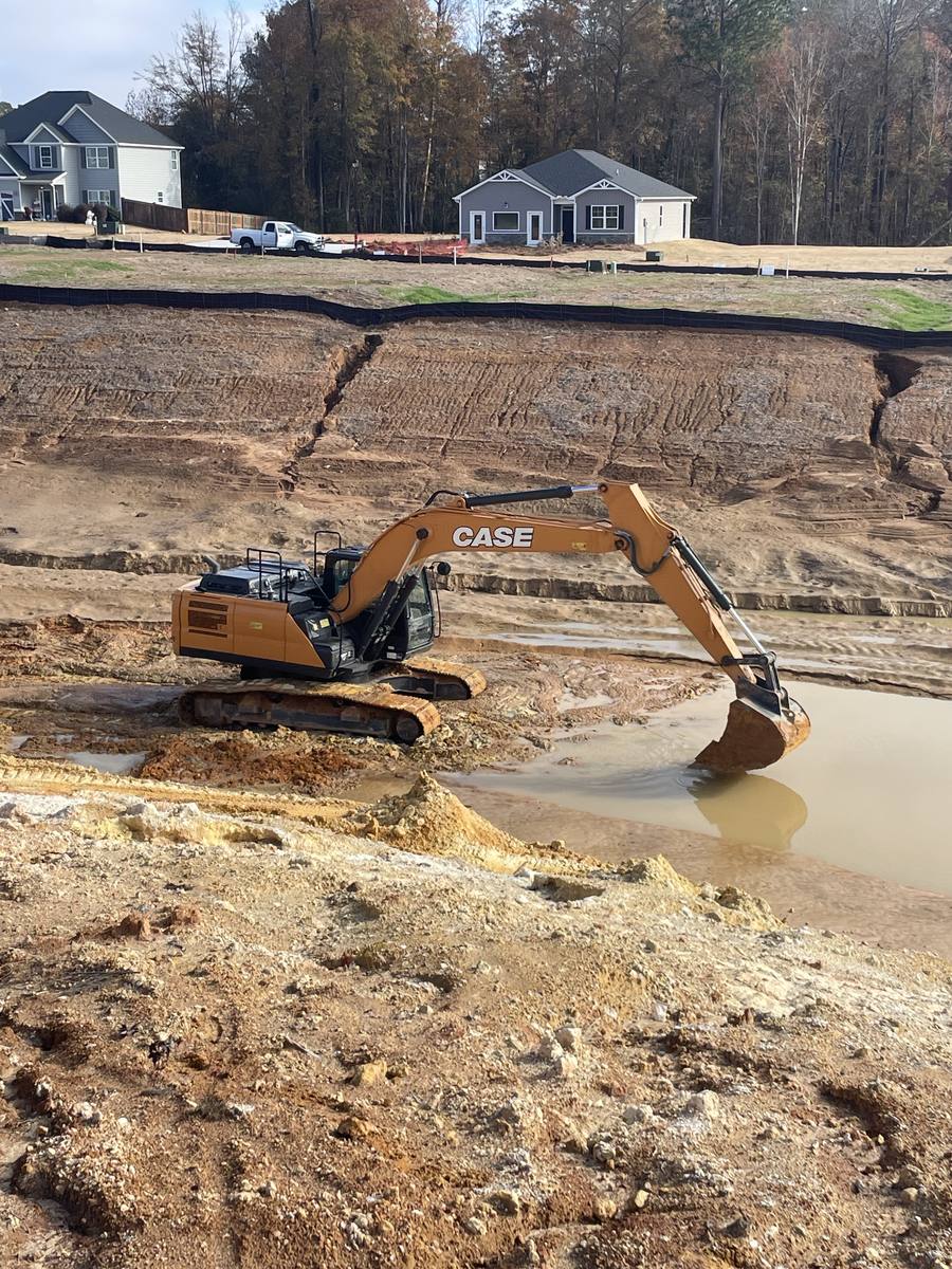 Excavator digging out a pond basin beside new homes